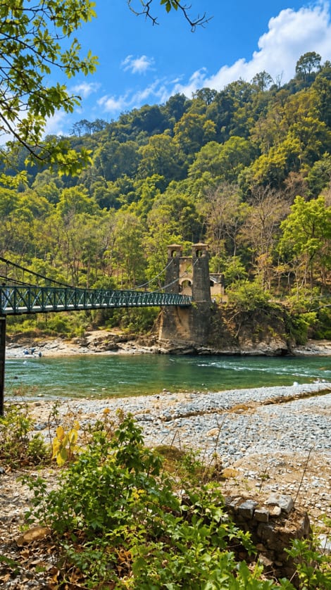 A suspension bridge spanning a river beneath wooded hills